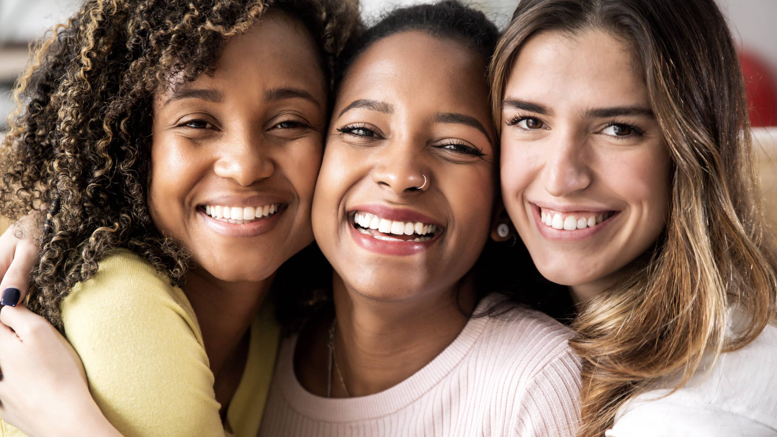 Three beautiful smiling girl friends hugging together - Multiracial group of women looking at camera