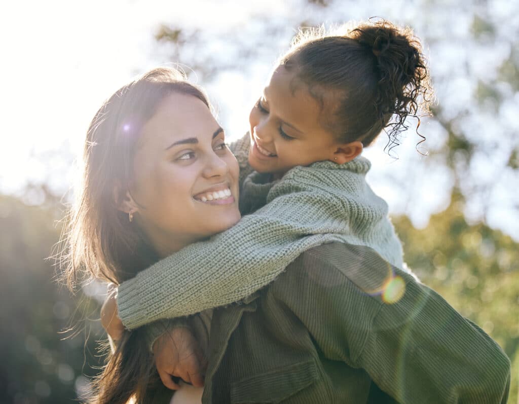 Woman with young girl riding piggy back smiling at each other.