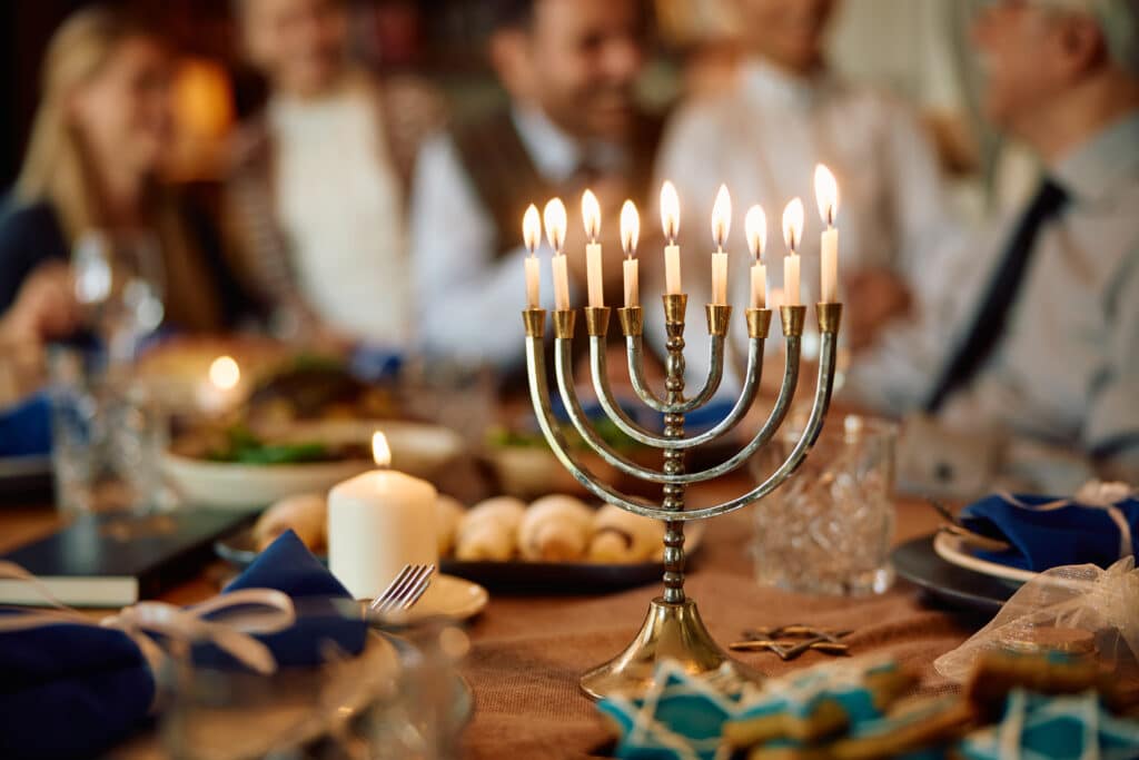 Lit candles in menorah with extended Jewish family in the background on Hanukkah.