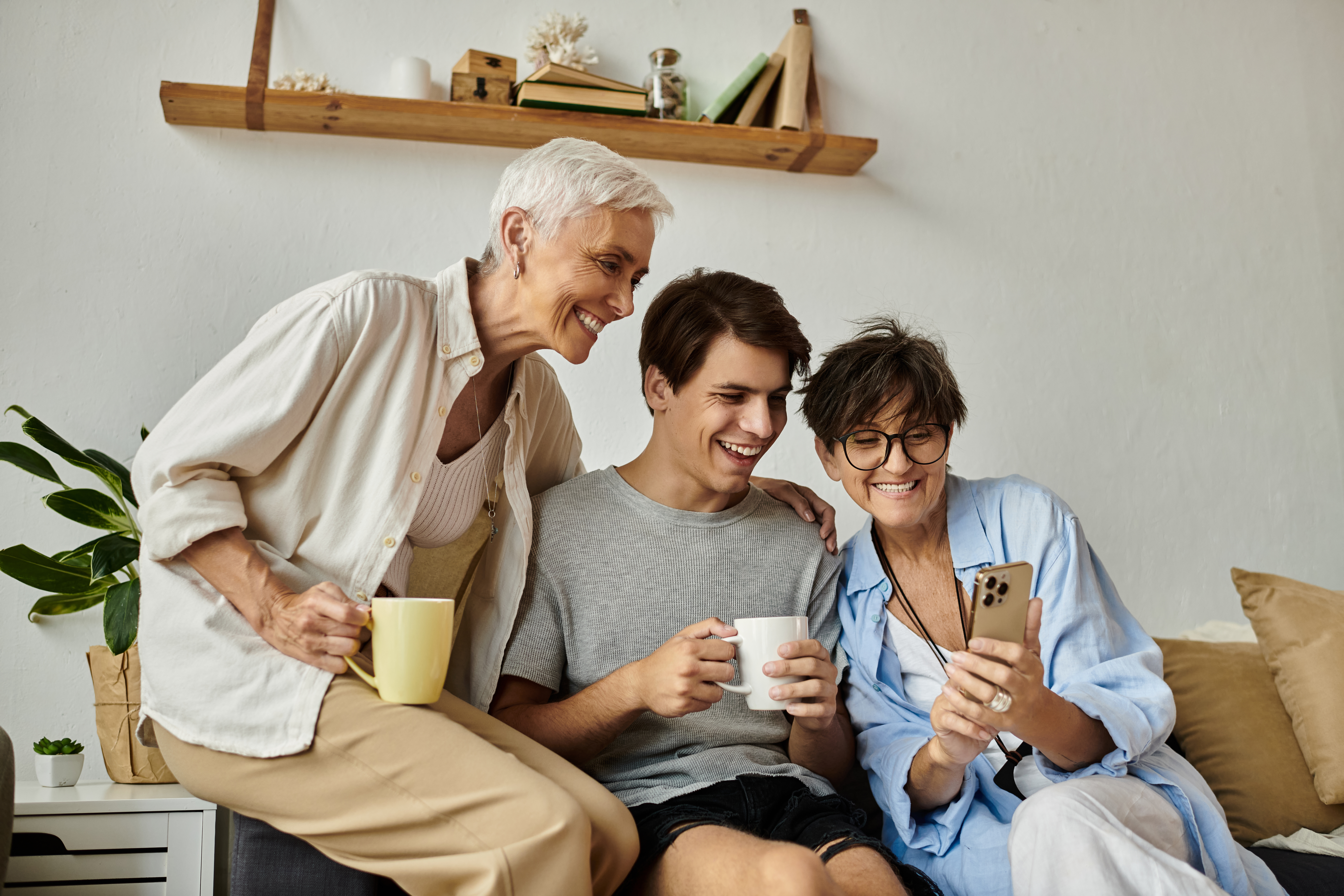 2 senior women look at smart phone with young adult man.