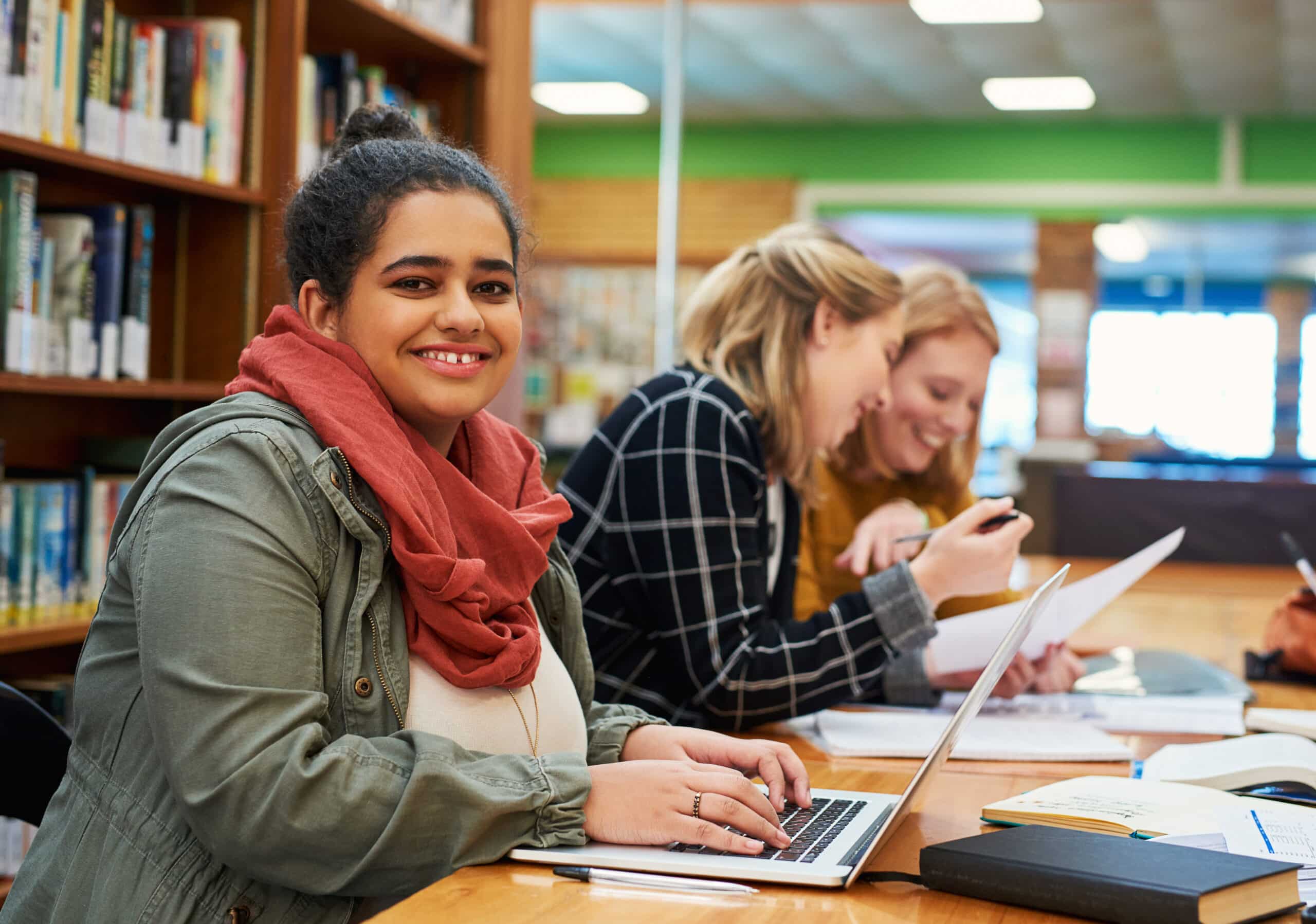 Portrait of a cheerful young female student working on her laptop and studying inside of a library
